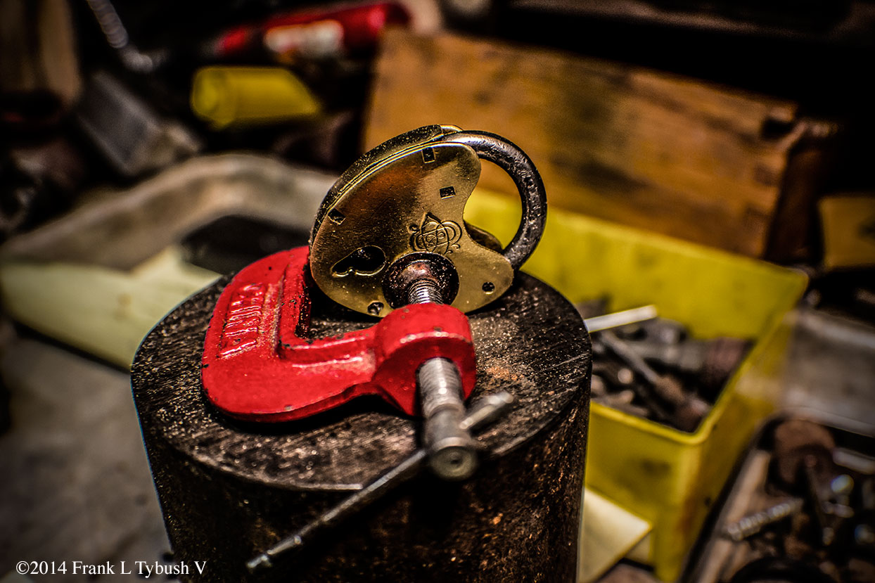 A red clamp that is holding together a brass lock in the shape of a heart/