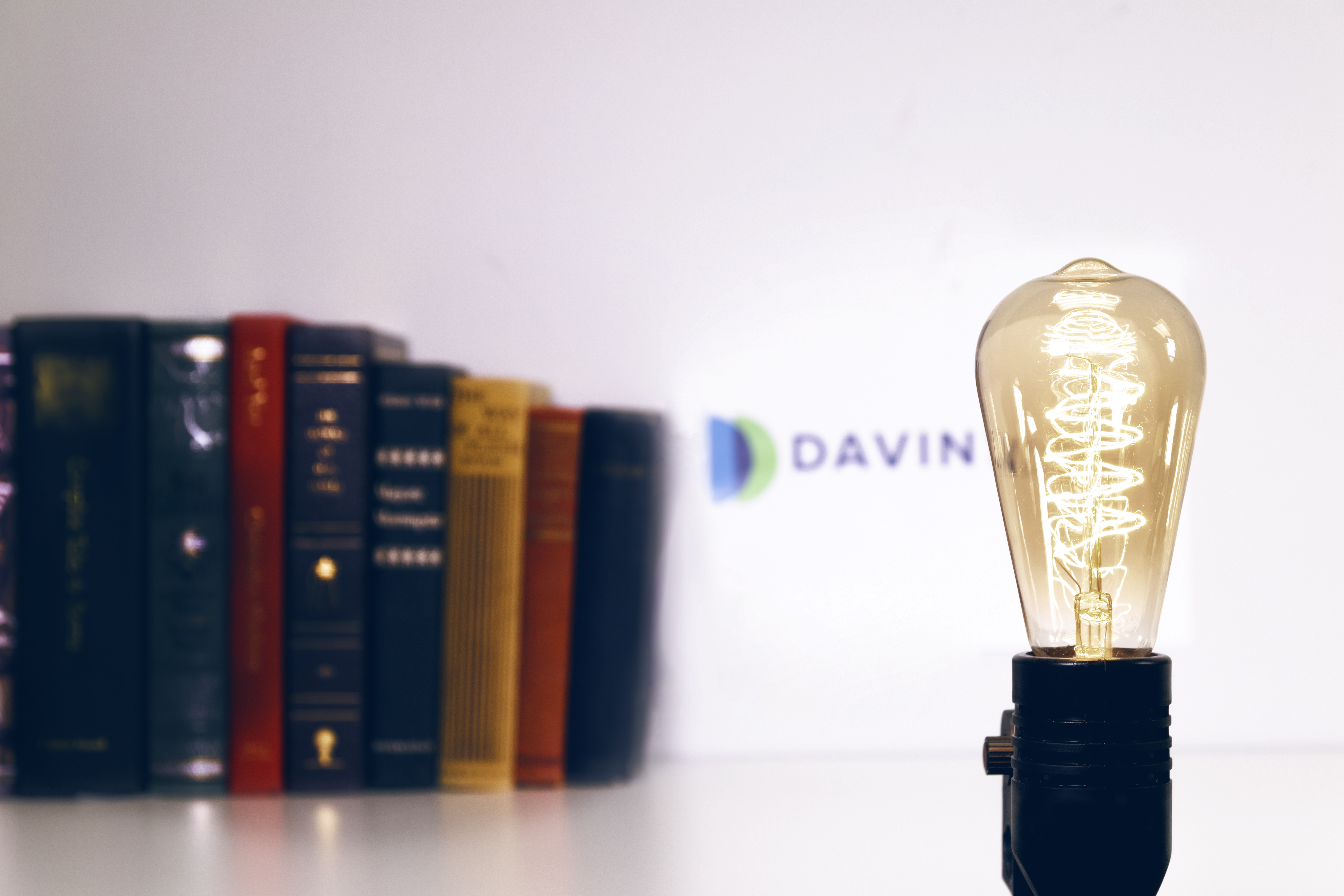 A lightbulb in the foreground with out of focus books and the word Davin.