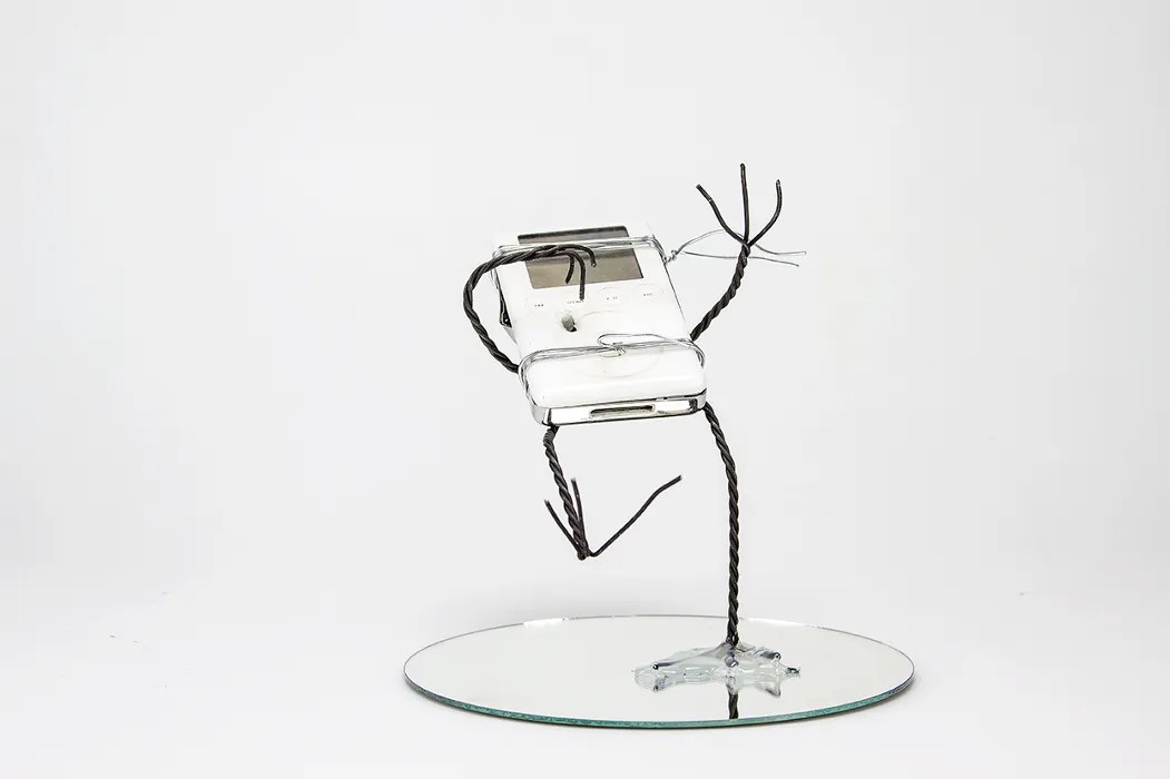 A wire sculpture of an anthropomorphized gen 2 ipod. It's shot with a bullet and falling backwards.