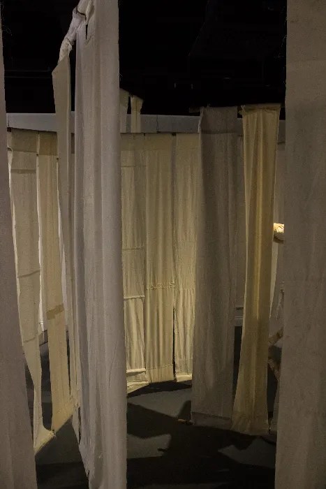 A photo from inside an art installation showing fabric panels hanging in a maze-like structure.
