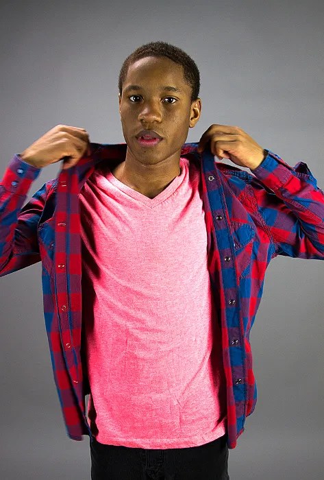 A young man looking directly at the camera. He's fixing his flannel shirt.