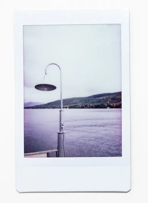 A polaroid of an older style lamp set in front of a lake.