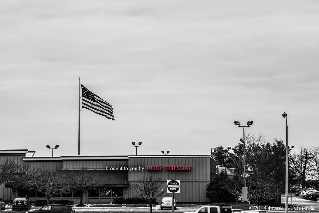 A black and white landscape photo of a Ruby Tuesday. The restaurant's logo is the only part of the image that's in color. Next to the logo, "Brought to you by" is overlayed on the image.